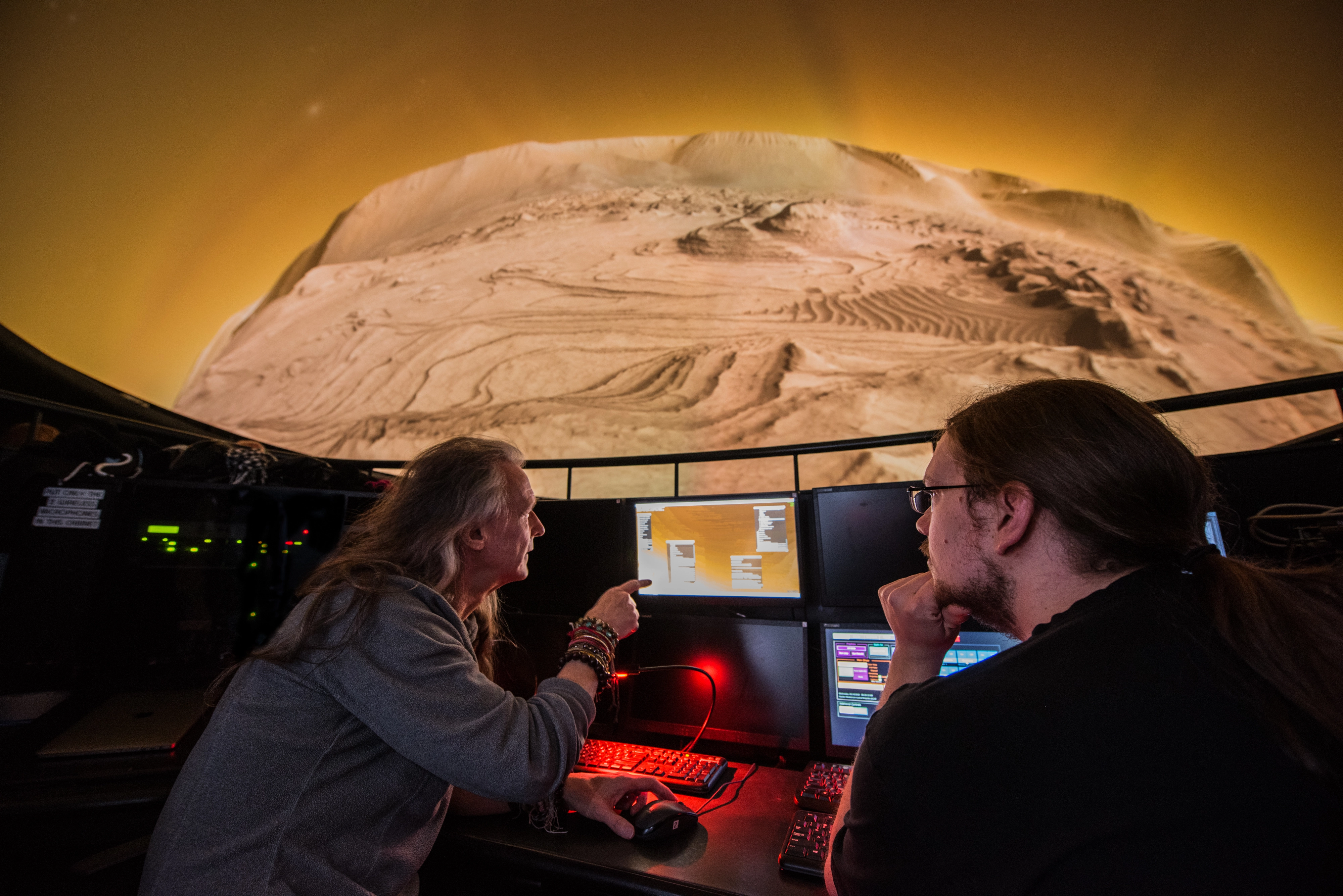 Two people at the Hayden Planetarium control console with Mars terrain projected on the dome